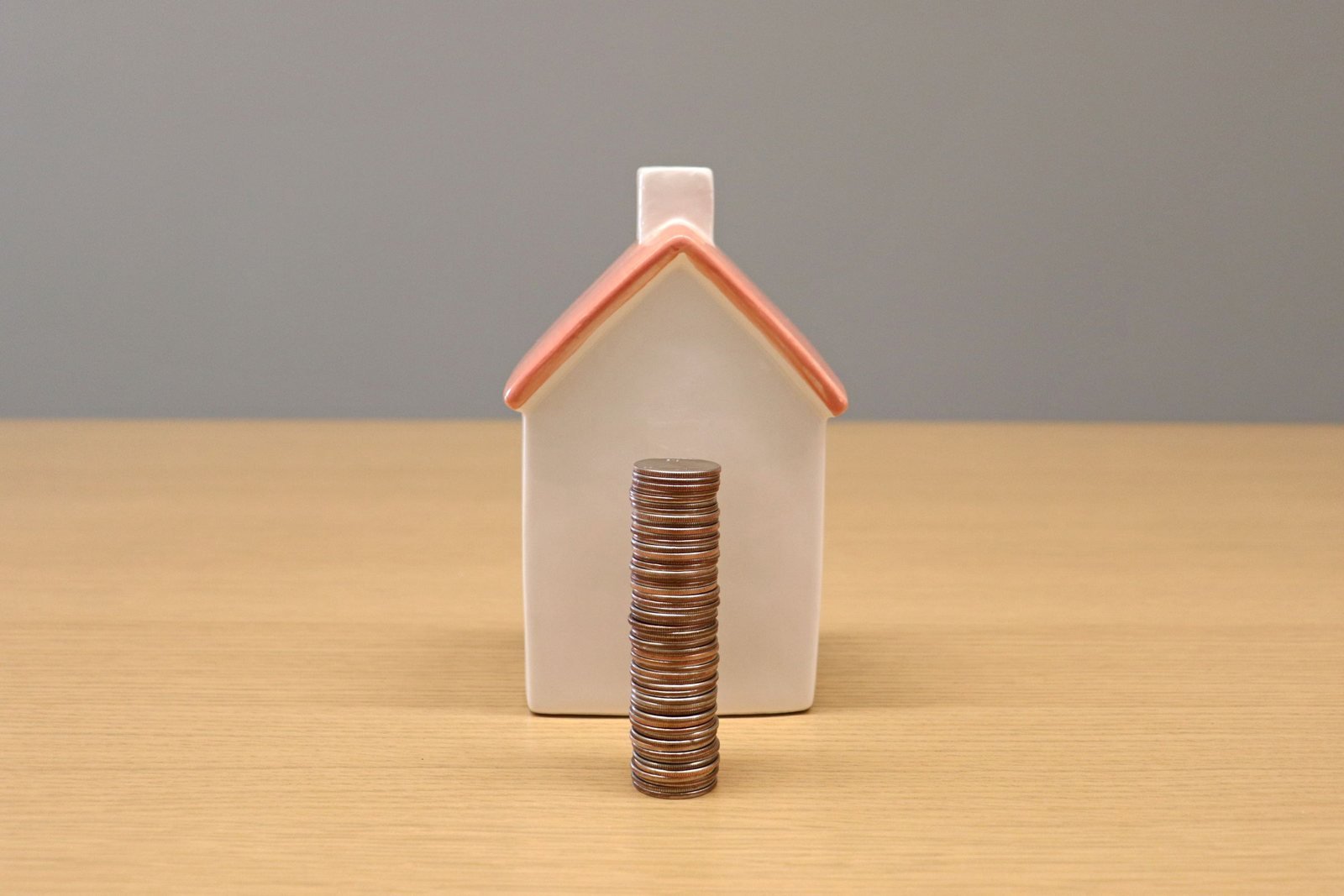 A house-shaped coin bank with a growing stack of coins in front of it